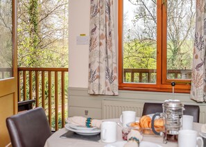 A dining area with a table set for breakfast, overlooking a garden with trees and a wooden deck.