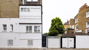 A residential street with a white two-story house, a tree, and a garage door. - Chic Apartment, Steps away from King's Rd Chelsea - Pass the Keys (London)