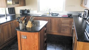Una cocina moderna con armarios de madera, encimera negra, isla integrada con bloque para cuchillos, ventana y campana extractora de acero inoxidable.