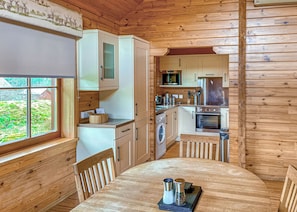 A wooden cabin interior with a dining table, kitchen area, and a view of the outdoors.