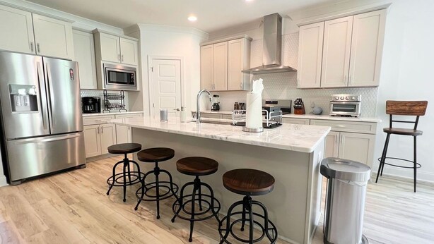 A modern kitchen with a central island, bar stools, stainless steel appliances, and a trash can. - Lots of amenities. Open Floor plan. Perfect for families and groups!  (Auburn)