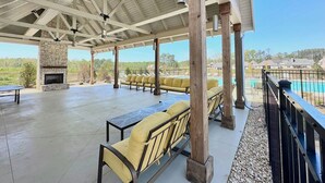 An outdoor patio with seating, a stone fireplace, and a pool in the background. - Lots of amenities. Open Floor plan. Perfect for families and groups!  (Auburn)