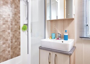 A bathroom with a shower, a sink with toiletries, and a mirror.