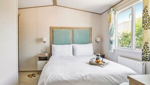 A neatly made bed with a headboard, bedside tables, a window with curtains, and a radiator.