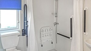 Ein Badezimmer mit Toilette, einer Dusche inklusive Haltegriff, einem Fenster und einem Waschbecken.