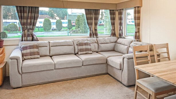 Un coin salon avec un canapé d’angle beige, une table à manger en bois et des chaises.