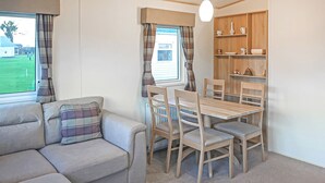 Une pièce chaleureuse avec un canapé, une table à manger et des chaises, un radiateur et une étagère ornée d’objets décoratifs.