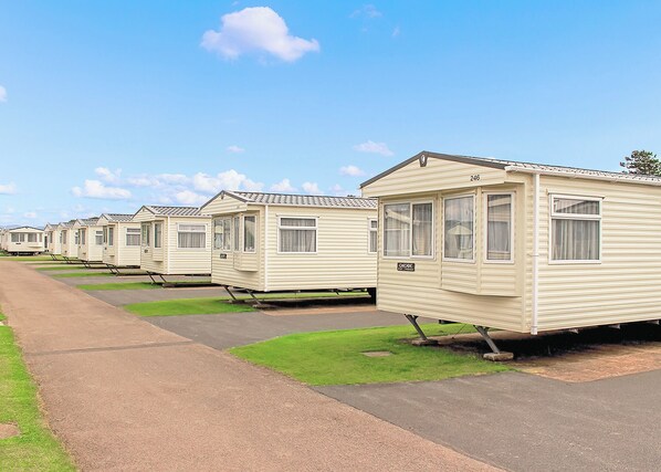A row of mobile homes with a paved walkway and green grass in front.