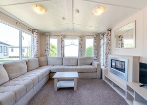 Un salon comprenant un canapé d’angle, une petite table, une cheminée et de grandes fenêtres avec des rideaux.