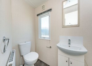 A bathroom with a toilet, a window, a sink, and a mirror. - Arundel Plus Caravan (Bognor Regis)
