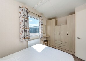 Una camera da letto con un letto, una finestra con tende, un termosifone, uno sgabello e un armadio.