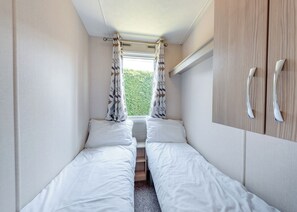 Une chambre compacte avec deux lits simples, une fenêtre avec des rideaux et une armoire à deux portes.