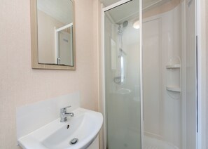 Un baño con lavamanos blanco, un espejo y cabina de ducha con paredes de vidrio.