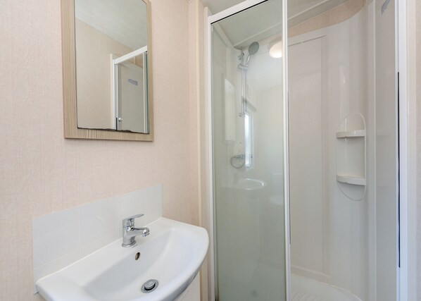 Un bagno con un lavandino bianco, uno specchio e una cabina doccia in vetro.