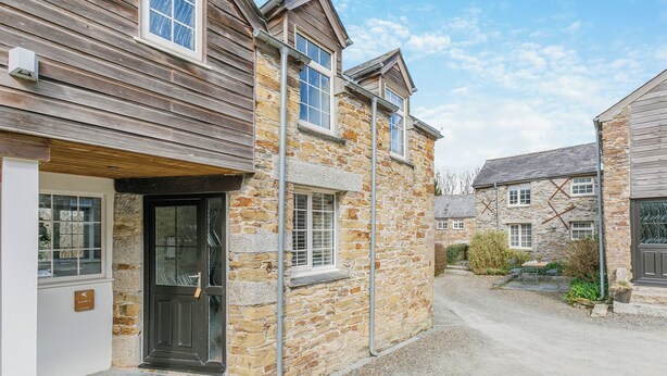 Un bâtiment en pierre avec une façade en bois, une allée gravillonnée et un ciel dégagé.