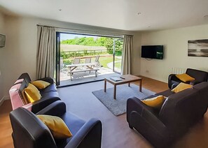 A living room with two sofas, a coffee table, a TV, and a sliding glass door leading to an outdoor patio with a table and chairs.