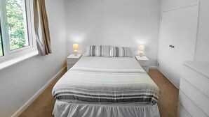 Ein Schlafzimmer mit einem großen Bett, zwei Nachttischen mit Lampen, einem Fenster mit Vorhängen und einer Tür.