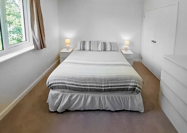 A bedroom with a large bed, two bedside tables with lamps, a window with curtains, and a door.