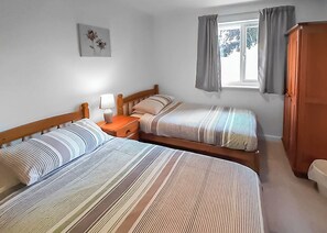 A room with two beds, a nightstand, a lamp, a window with curtains, and a wardrobe.