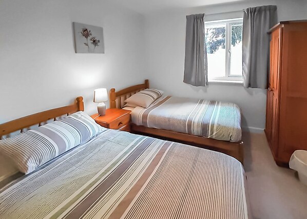 A room with two beds, a nightstand, a lamp, a window with curtains, and a wardrobe. - Single storey cottage in its own secluded setting away from the lodges. (North Tamerton, Bude)