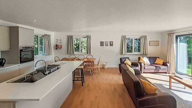 Eine moderne Küche mit einer zentralen Kochinsel, einem Essbereich mit Stühlen, einer Couch und einem großen Fenster.