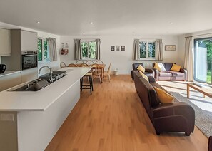 A modern kitchen with a central island, dining area with chairs, a sofa, and a large window.