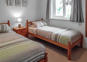 Een slaapkamer met twee eenpersoonsbedden, een nachtkastje met een lamp, een raam met gordijnen en wanddecoratie.