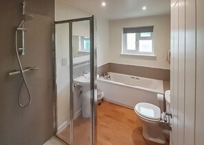A bathroom with a glass shower enclosure, a bathtub, a toilet, and a window.