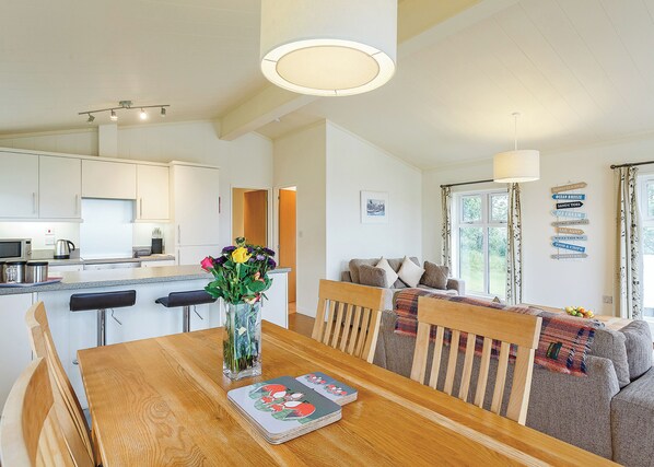 A modern kitchen with white cabinets, a dining table with a vase of flowers, and a cozy living area with a sofa and a view of the outdoors. - 2 bedroom accommodation in Carnmenellis, Nr Falmouth (Carnmenellis, Nr Falmouth)