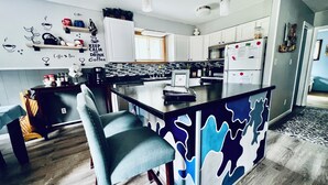 Una cocina moderna con una isla central, taburetes de bar y una obra de arte con motivos de café.