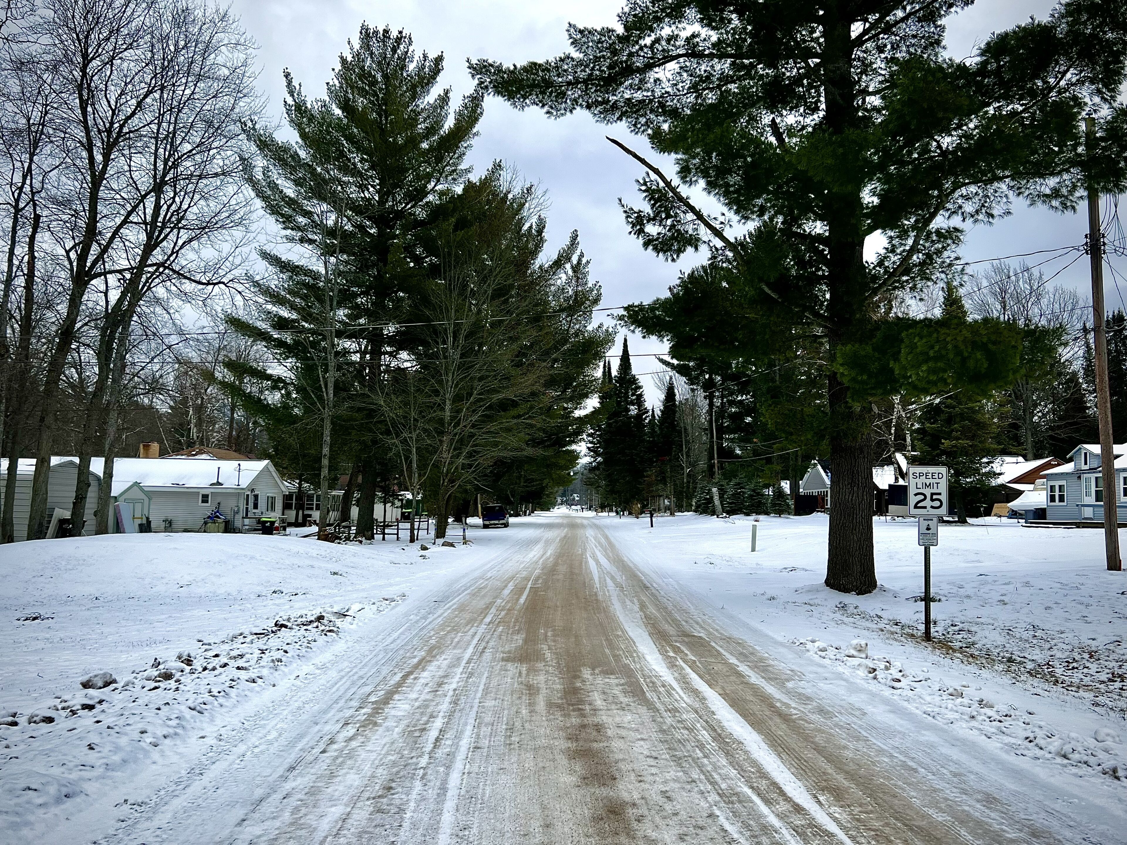 Une route enneigée bordée d’arbres et de maisons.