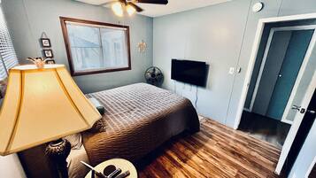 Un dormitorio con cama, ventilador de techo, televisor, lámpara, reloj y puerta.