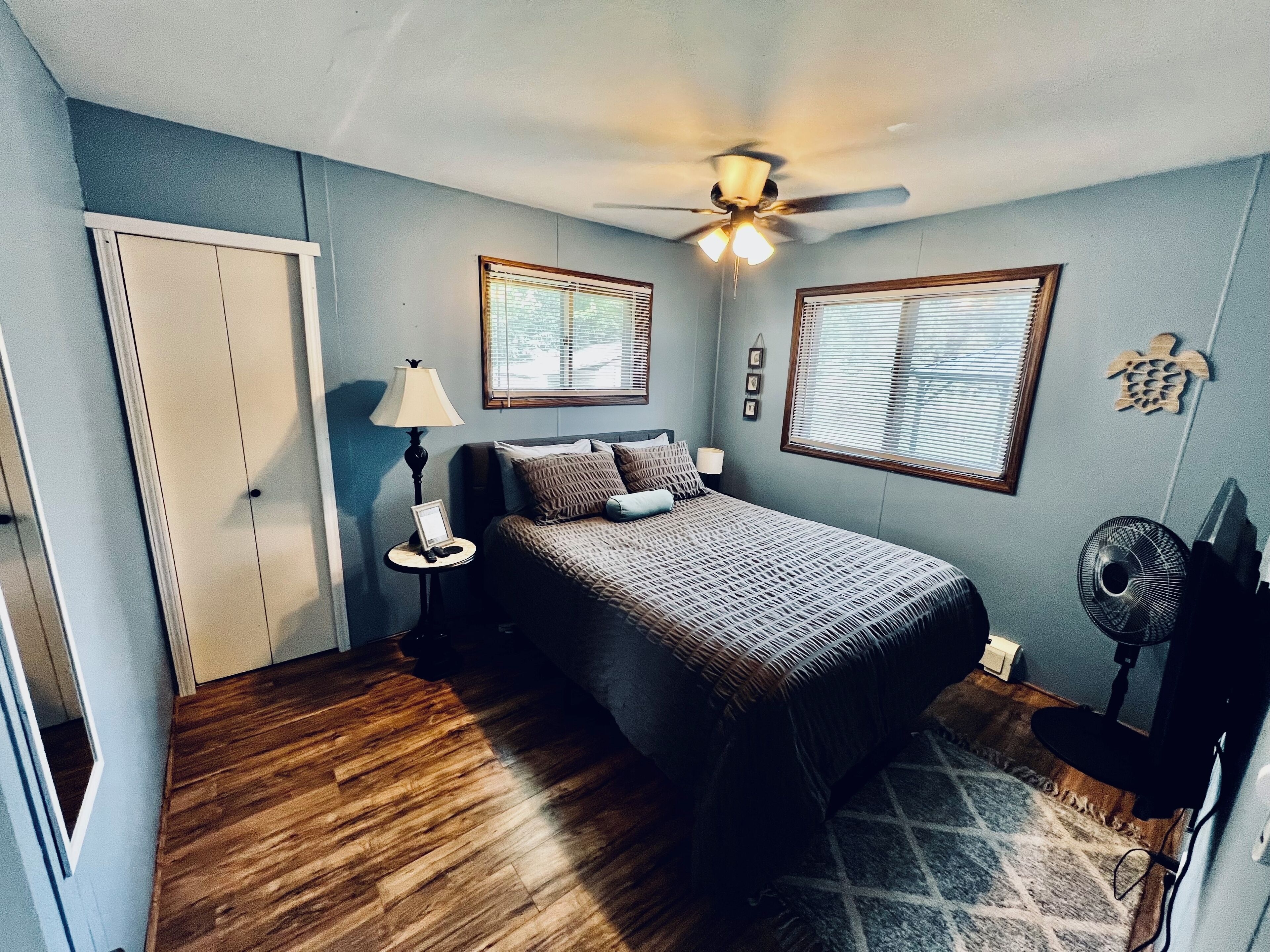 A bedroom with a bed, two bedside tables, a ceiling fan, and a window with blinds.
