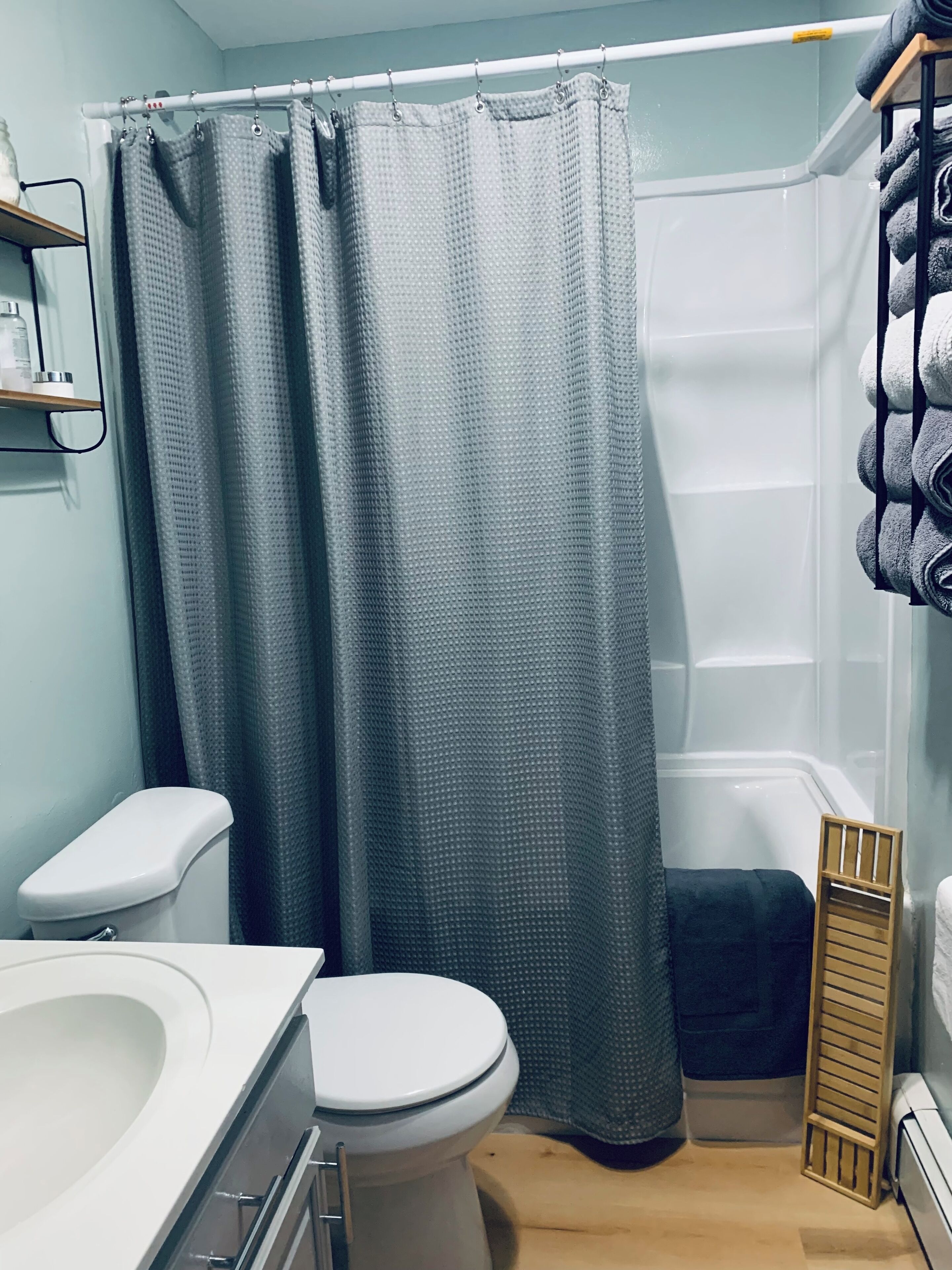 A bathroom with a toilet, a shower curtain, a towel rack, and a small shelf.