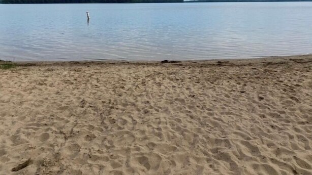 Una playa arenosa con un cuerpo de agua tranquilo y una línea de costa distante.