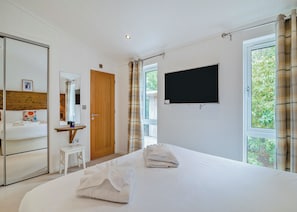 Ein Schlafzimmer mit Bett, Nachttisch, Spiegel, Fernseher und einem Fenster mit Vorhängen.