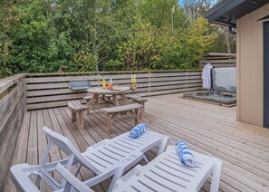 Eine Holzterrasse mit Tisch, Stühlen, einem Grill und einem Whirlpool.