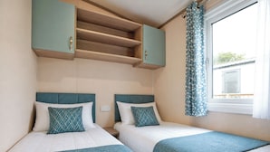 Un dormitorio con dos camas, una ventana con cortinas y una estantería empotrada sobre las camas.