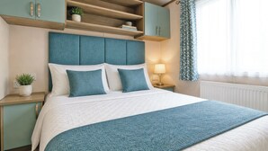 Un dormitorio con cama, mesita de noche, lámpara, ventana con cortinas y estanterías empotradas sobre la cama.