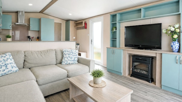 Una sala de estar moderna con sofá, televisor, chimenea y zona de cocina.