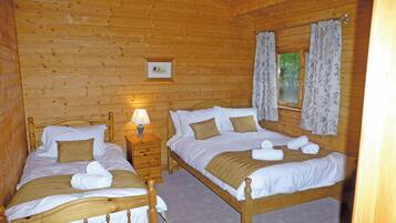 Une chambre dans un chalet en bois, avec deux lits, une table de chevet, une lampe et un tableau encadré au mur.