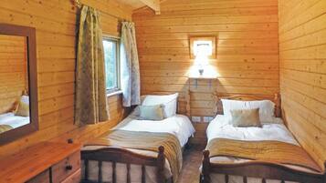 Une chambre de style cabane avec deux lits en bois, une commode, un miroir et une fenêtre avec des rideaux.