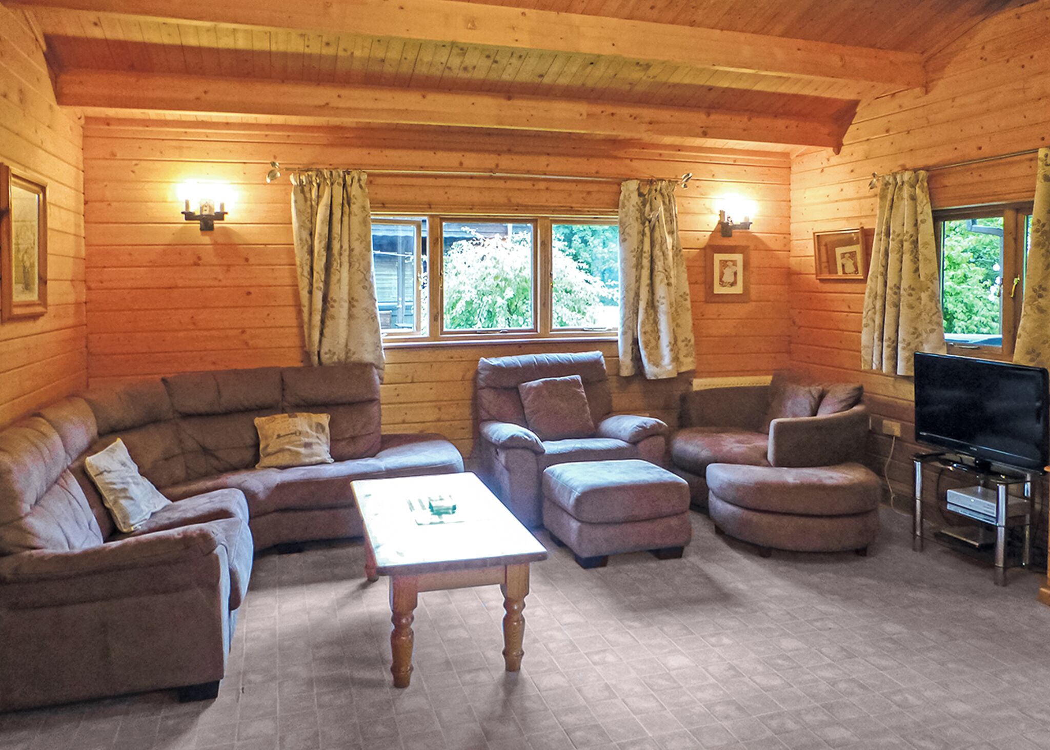 L’intérieur d’une cabane en rondins, avec un ensemble de canapés, un pouf, une table basse et un téléviseur posé sur un meuble.