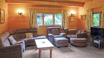 L’intérieur d’une cabane en rondins, avec un ensemble de canapés, un pouf, une table basse et un téléviseur posé sur un meuble.