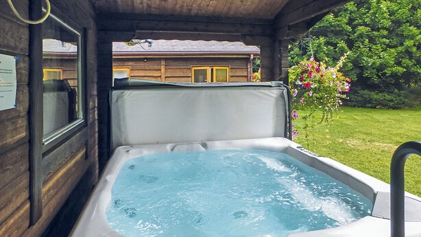 A hot tub with a view of a wooden cabin and a garden. - Spacious timber lodge with one double and one single in one room. (Kentisbeare, Nr Cullompton)