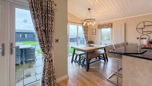 A modern kitchen with a black countertop, a dining area with a wooden table and chairs, and a large window with patterned curtains. - 4 bedroom accommodation in Tenby (Tenby)