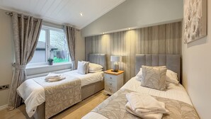 A bedroom with two beds, a window with curtains, a bedside table with a lamp, and a headboard. - 4 bedroom accommodation in Tenby (Tenby)