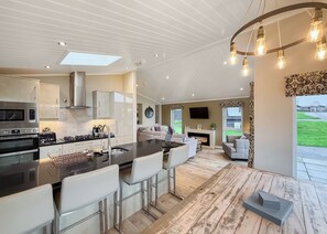 A modern kitchen with a central island, bar stools, a dining area with a fireplace, and a living room with a TV. - 4 bedroom accommodation in Tenby (Tenby)