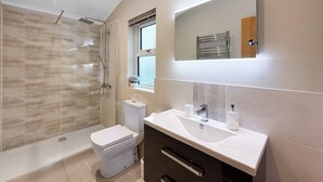 A modern bathroom with a glass shower enclosure, a toilet, a vanity with a mirror, and a window. - 4 bedroom accommodation in Tenby (Tenby)