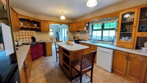 A kitchen with wooden cabinets, a central island, a sink, and a refrigerator. - Cuckoo Tree House, Glengarriff, Beara Peninsula (Glengarriff)